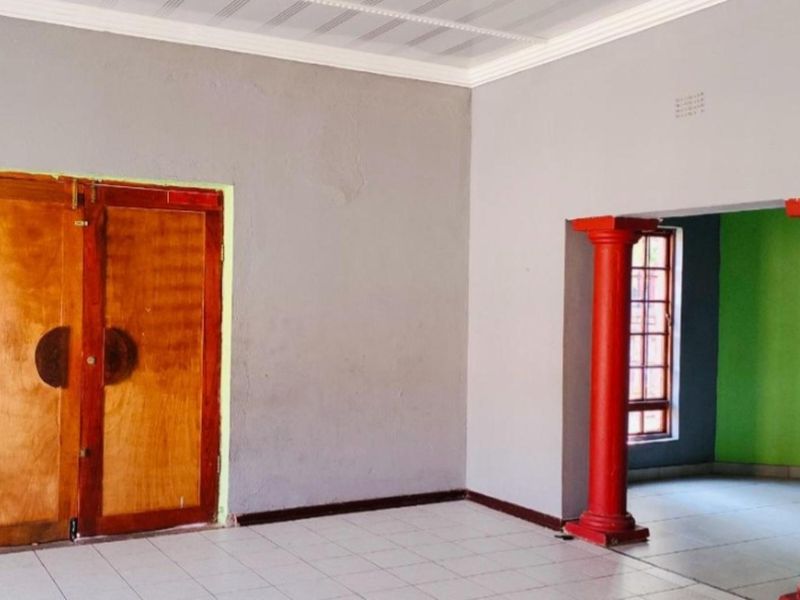 An empty living area featuring tiled floors, decorative red columns, and double wooden doors, offering a blank canvas for interior design updates.