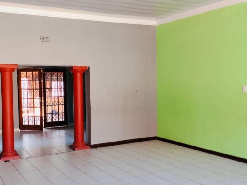 An empty living area featuring tiled floors, decorative red columns, and a security gate leading to an adjacent space.