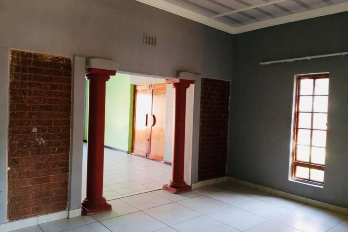 An empty living area featuring decorative columns, exposed brick accents, tiled flooring, and a timber-framed window, offering a blank canvas for renovation.