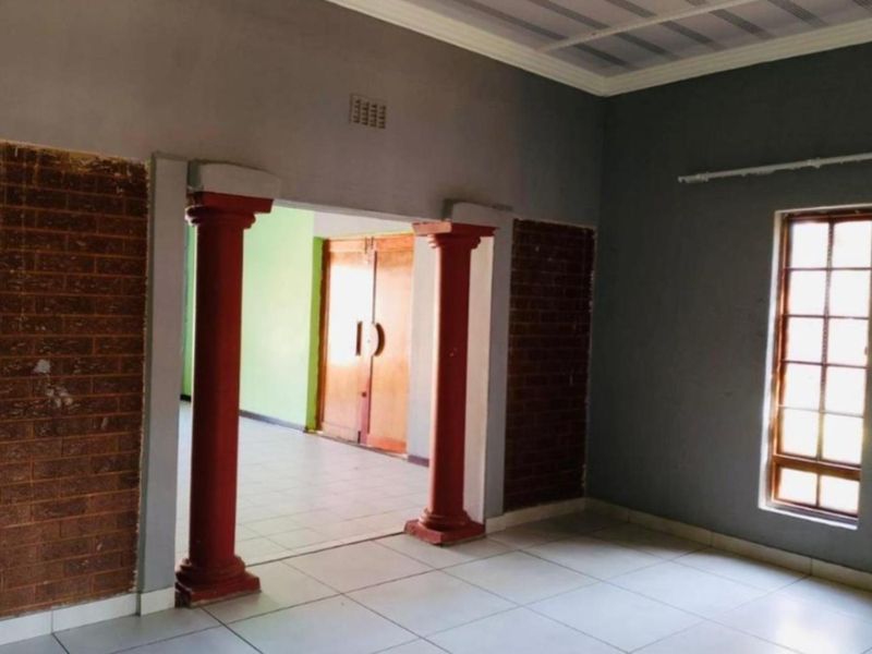 An empty living area featuring decorative columns, exposed brick accents, tiled flooring, and a timber-framed window, offering a blank canvas for renovation.