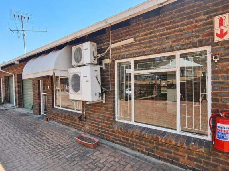 Exterior view of a face brick townhouse featuring security bars, wall-mounted air conditioning units, and paved driveway access.