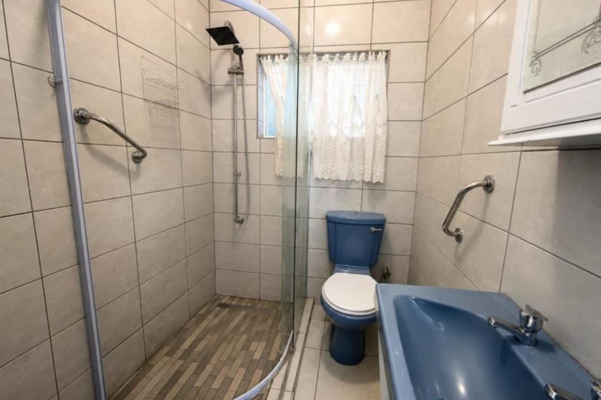 A functional bathroom featuring a walk-in shower with glass enclosure, grab rails for accessibility, and tiled finishes throughout.