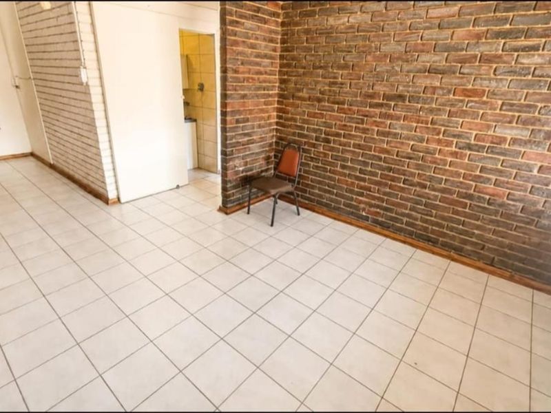 Spacious living area featuring a prominent exposed brick feature wall and neutral ceramic floor tiling, offering a versatile blank canvas for interior design.
