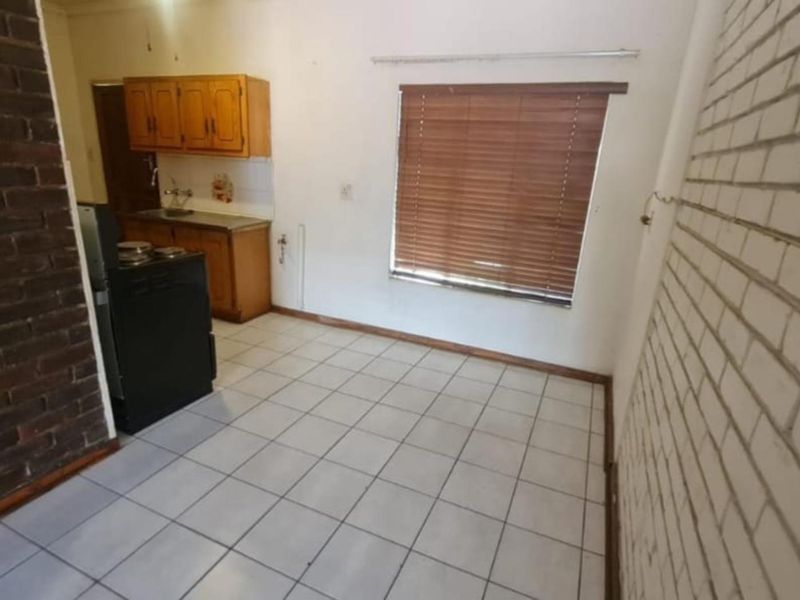A compact kitchen featuring tiled flooring, exposed brick accents, and dated wooden cabinetry, offering a functional space ready for modernization.