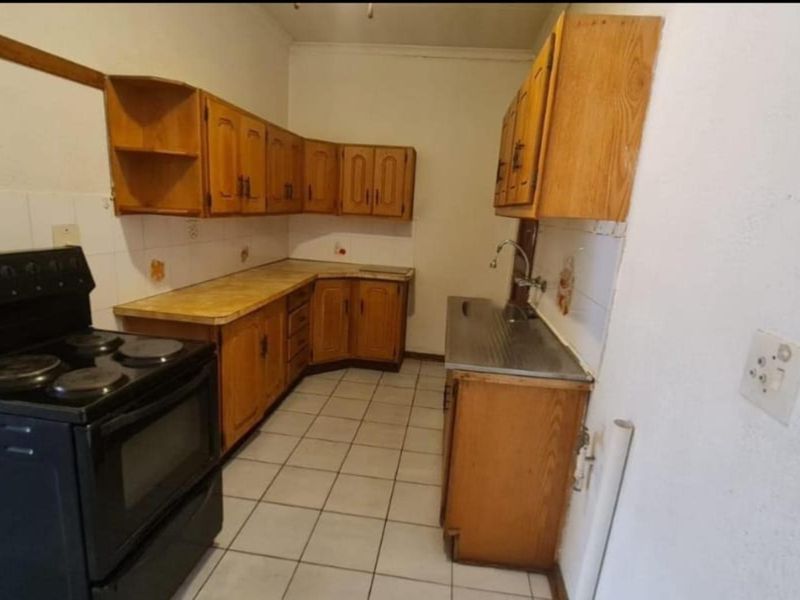 A dated kitchen featuring wooden cabinetry, laminate countertops, a stainless steel sink, and tiled flooring, offering a functional layout ready for modernization.
