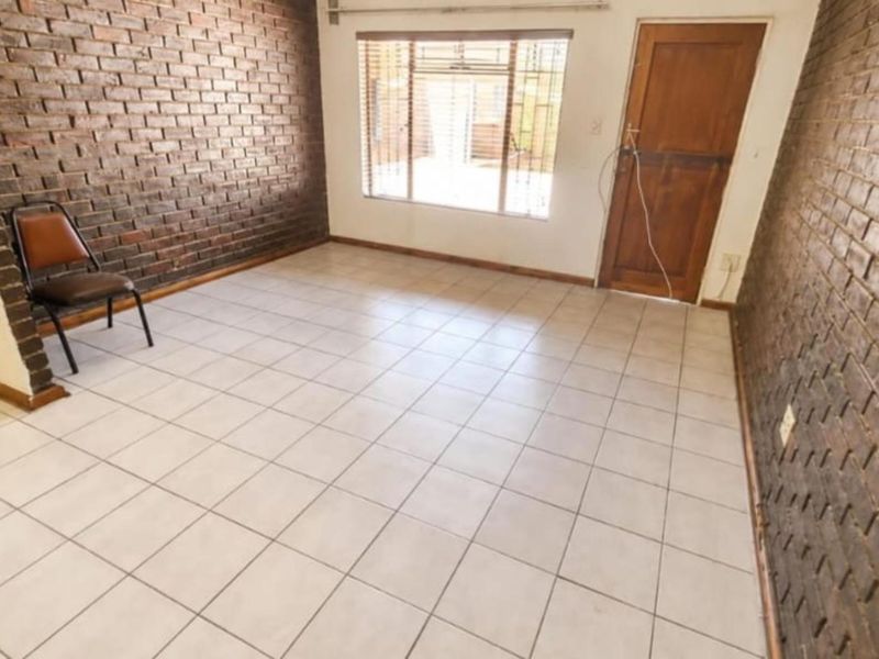 Spacious living area featuring distinctive exposed brick walls, neutral ceramic floor tiles, and direct access to the exterior via a timber door.