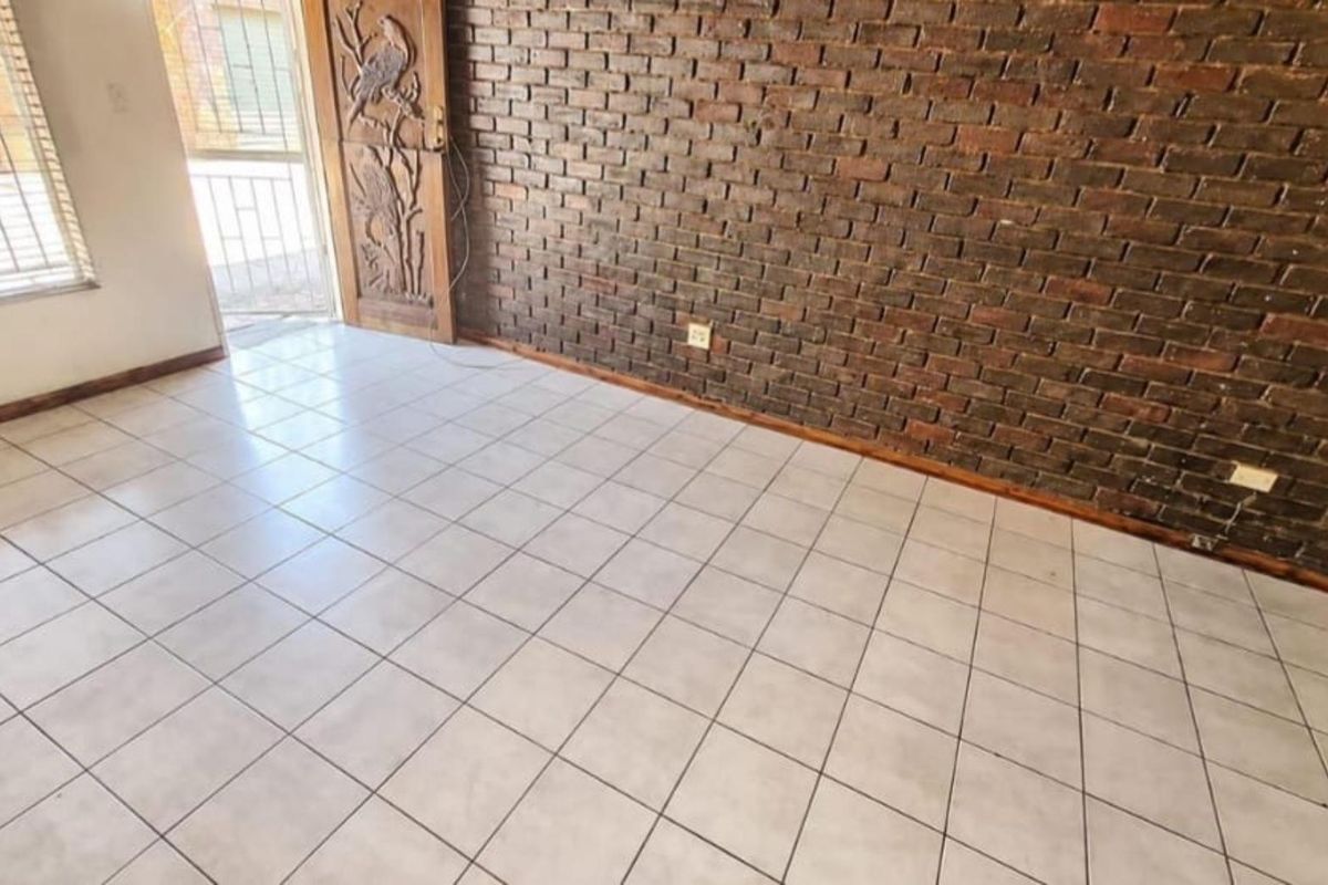 An empty living area featuring a prominent exposed brick wall, ceramic tiled flooring, and a decorative carved wooden entrance door.