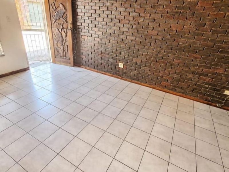 An empty living area featuring a prominent exposed brick wall, ceramic tiled flooring, and a decorative carved wooden entrance door.
