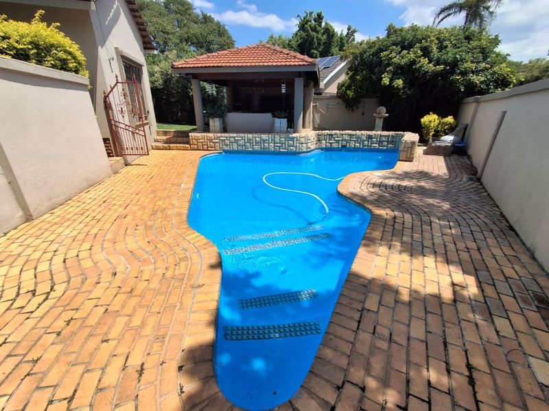 Outdoor pool area featuring a swimming pool with brick paving surround and a covered patio structure.