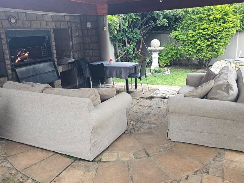 Covered outdoor patio featuring a built-in braai, timber ceiling, and stone paved flooring, overlooking a private garden area.