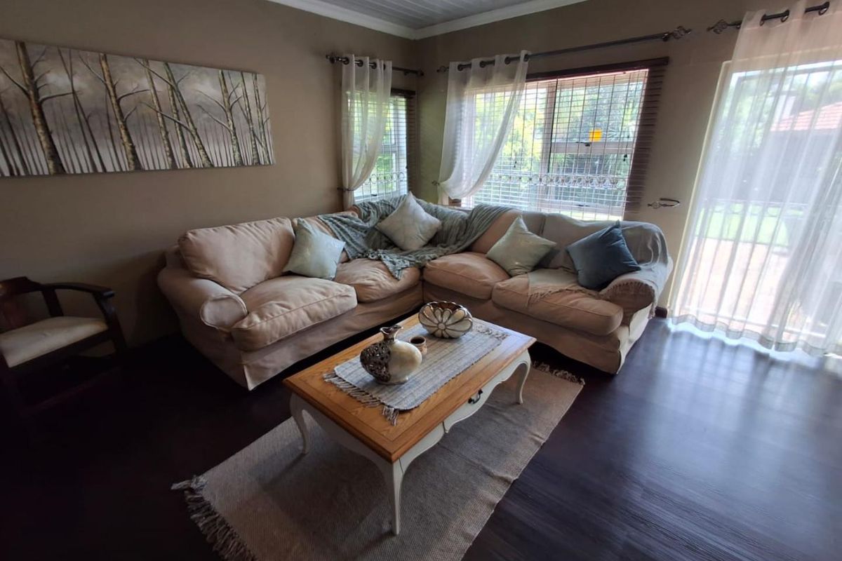A comfortable living room featuring dark laminate flooring, a tongue and groove ceiling, and large windows with security bars and access to the outdoors.