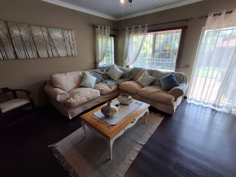 A comfortable living room featuring dark laminate flooring, a tongue and groove ceiling, and large windows with security bars and access to the outdoors.
