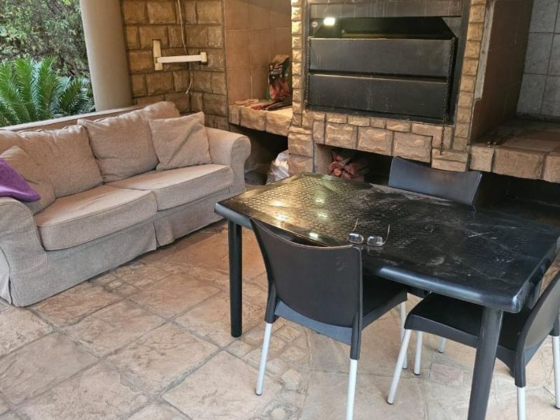 Covered outdoor patio featuring a built-in braai, stone cladding, and stone paved flooring, providing a functional space for outdoor entertainment.