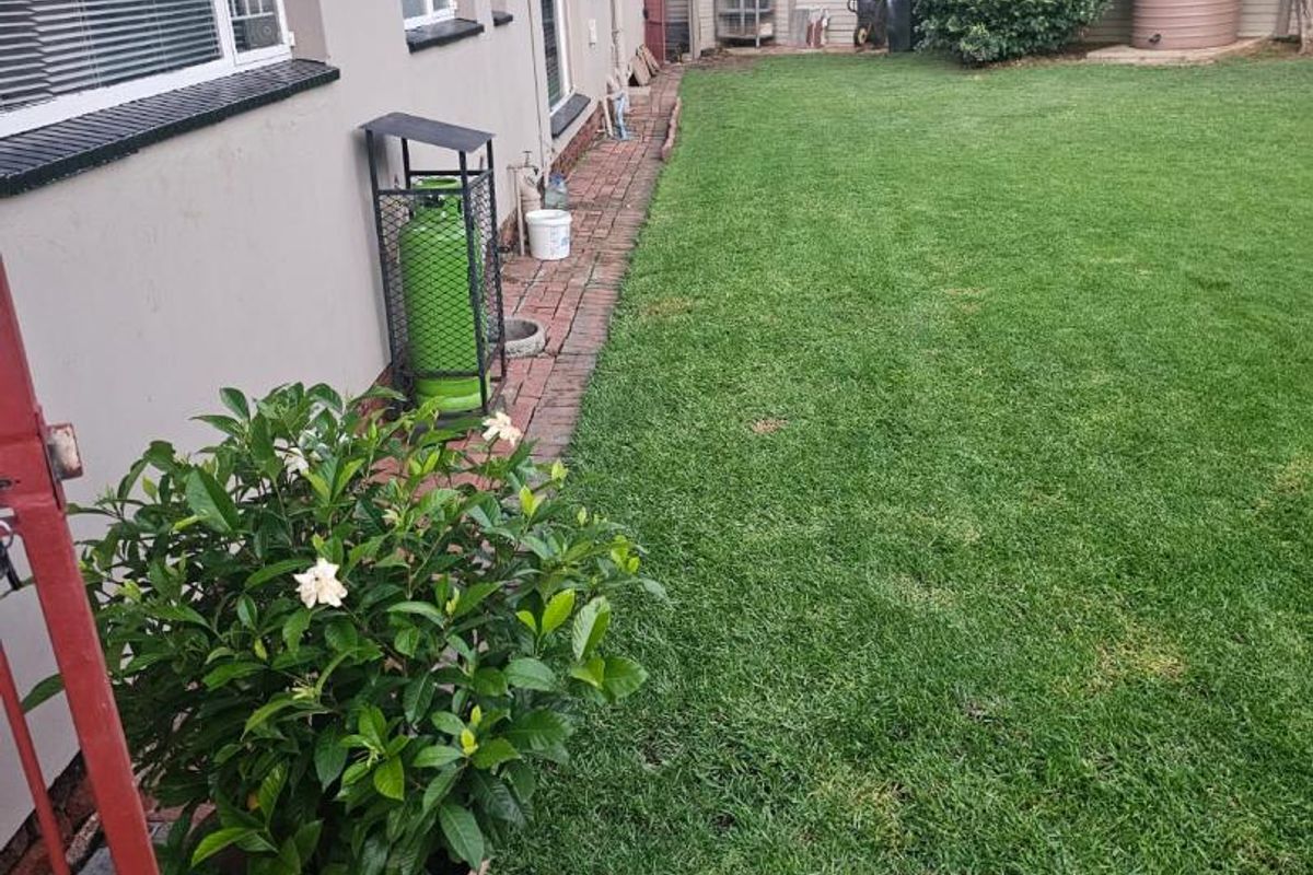 A well-maintained rear garden featuring a brick-paved walkway, lush green lawn, and a water storage tank along the boundary fence.