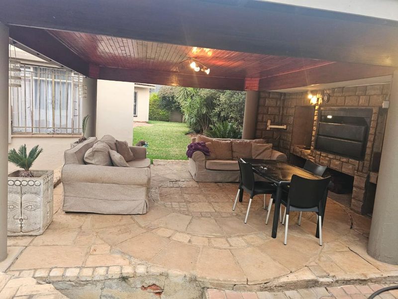 Covered outdoor patio featuring a built-in braai, stone cladding, and timber ceiling, overlooking the garden area.