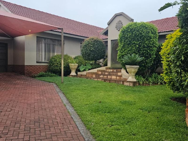 Front elevation of a well-maintained house featuring a brick paved driveway, shade sail carport, and landscaped garden leading to the main entrance.