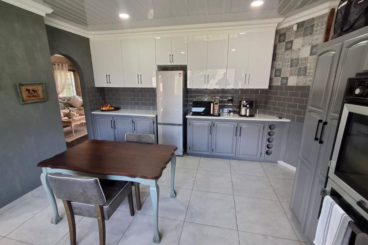 Modern kitchen featuring two-tone cabinetry, subway tile backsplash, patterned accent wall, and integrated oven, with an adjacent dining area.