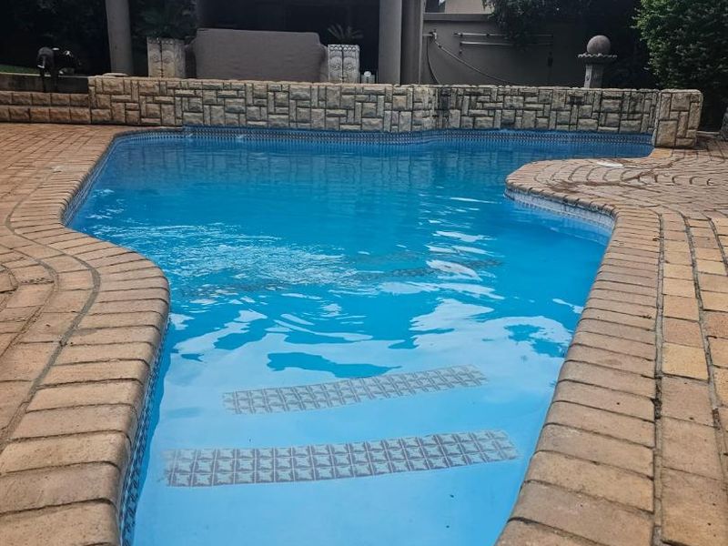 A well-maintained swimming pool with brick coping and a stone-clad retaining wall, featuring an adjacent covered patio area.