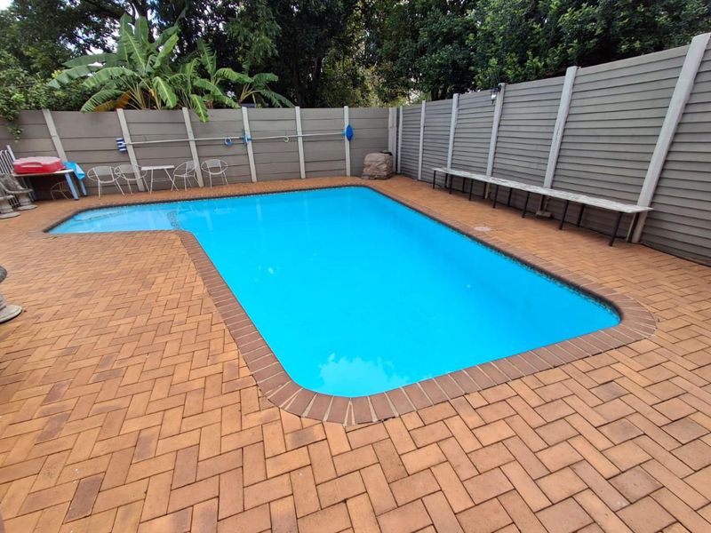A well-maintained outdoor swimming pool area featuring brick paving, a perimeter boundary fence, and a built-in bench for seating.
