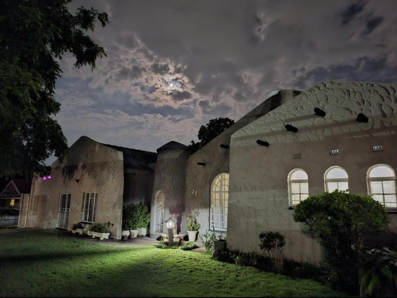 Night view of the front elevation featuring a unique textured stucco facade, arched windows, and a well-maintained front lawn.
