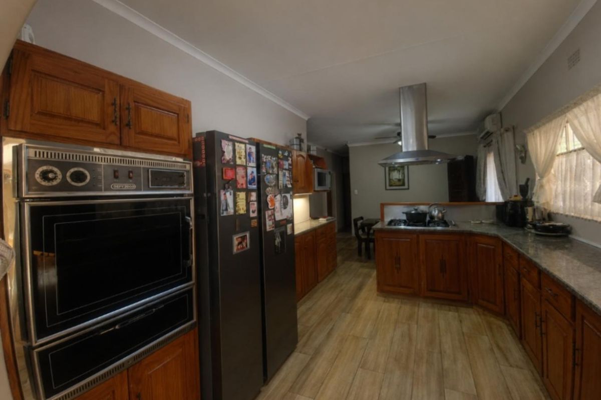 Spacious kitchen featuring wooden cabinetry, granite countertops, built-in oven, and a modern extractor fan, with durable laminate flooring throughout.