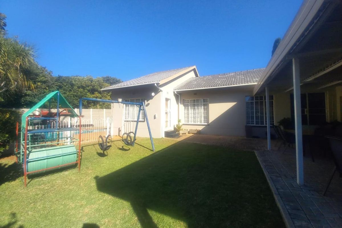 Rear view of the property featuring a paved patio, covered veranda, and a well-maintained garden area with a tiled roof structure.