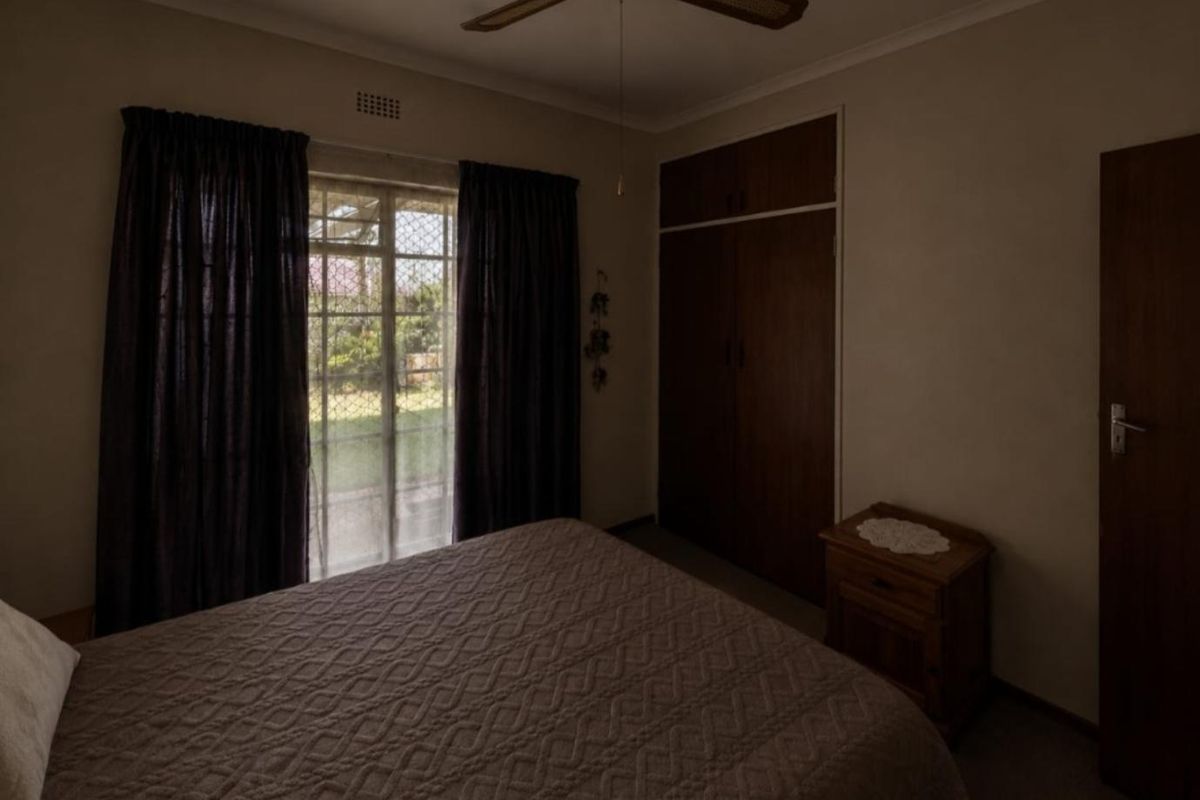 A bedroom featuring built-in cupboards, a ceiling fan, and a security gate leading to the exterior.