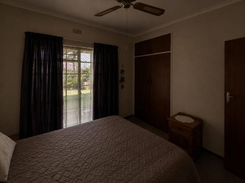 A bedroom featuring built-in cupboards, a ceiling fan, and a security gate leading to the exterior.
