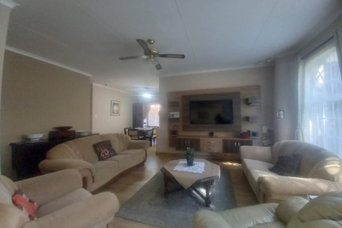 Spacious living room featuring laminate flooring, a ceiling fan, and a built-in media wall unit, offering a comfortable and functional family space.