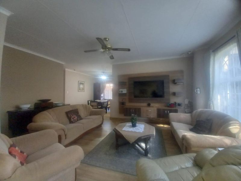 Spacious living room featuring laminate flooring, a ceiling fan, and a built-in media wall unit, offering a comfortable and functional family space.