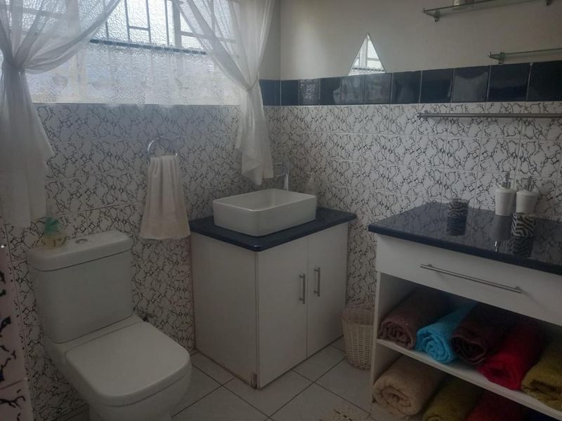 A functional bathroom featuring a vessel sink, granite-topped vanity cabinet, tiled walls, and standard toilet fixtures.
