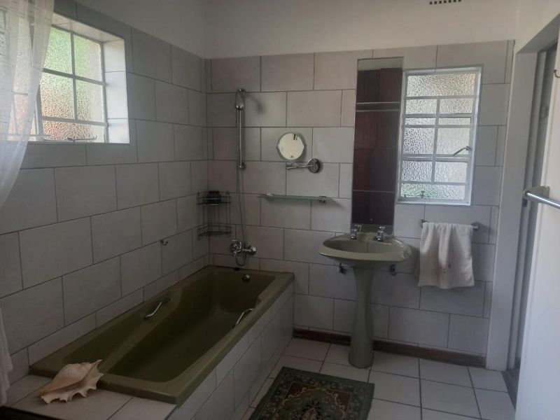A functional bathroom featuring a built-in bathtub, pedestal sink, and tiled finishes, offering a classic layout with potential for modern updates.