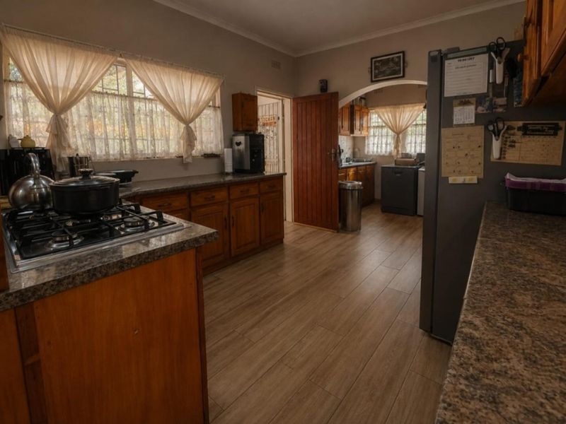 A functional kitchen featuring wooden cabinetry, granite countertops, and a gas hob, with an adjoining scullery area accessible through an archway.