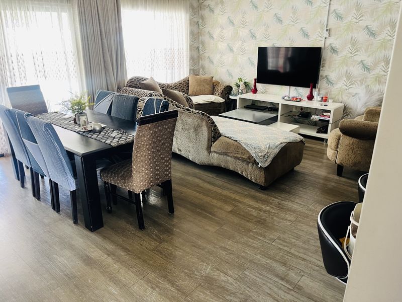 An open-plan living and dining area featuring wood-look laminate flooring, patterned wallpaper, and large sliding glass doors providing natural light.