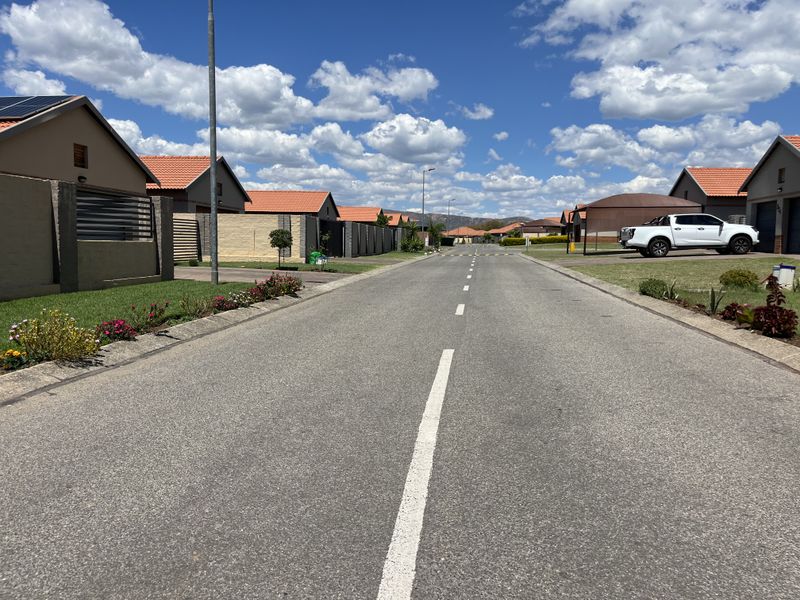 A clear street view of a residential estate featuring paved roads, well-maintained boundary walls, and modern homes with tiled roofs.