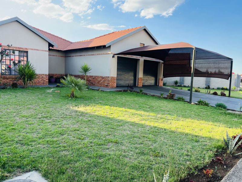 Front view of a well-maintained house featuring a double garage, paved driveway with a shade cloth carport, and a neat front lawn.