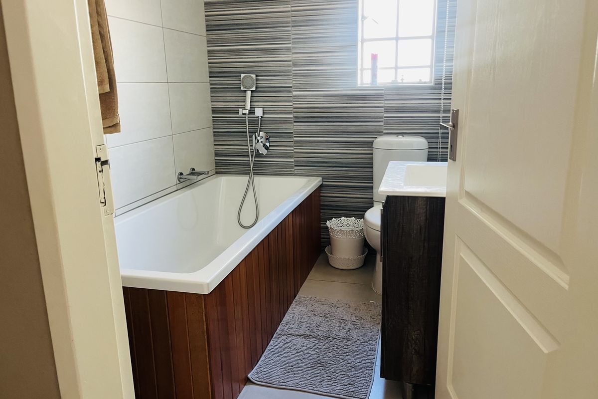 A compact bathroom featuring a bathtub with wood-panelled side, a modern vanity unit, and a toilet, accented with decorative striped wall tiling.