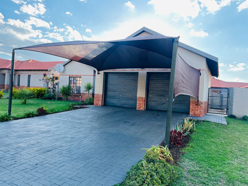 Front view of the property featuring a paved driveway, double garage with metal doors, and a protective shade sail structure.