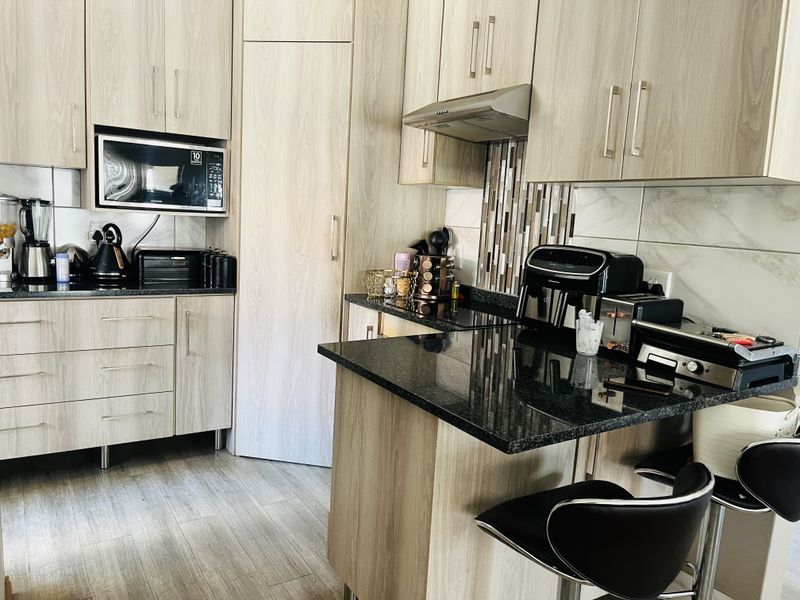 Modern kitchen featuring light wood-grain cabinetry, dark granite countertops, built-in microwave, and a sleek extractor fan with tiled backsplash.