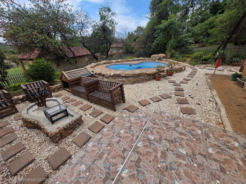 Outdoor entertainment area featuring a raised stone-clad swimming pool, a matching stone fire pit, and paved patio space set within a landscaped garden.