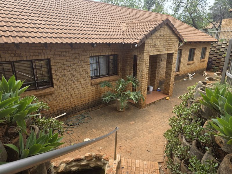 Rear view of a face brick house featuring a paved patio area, tiled roof, and tiered garden landscaping with a retaining wall.