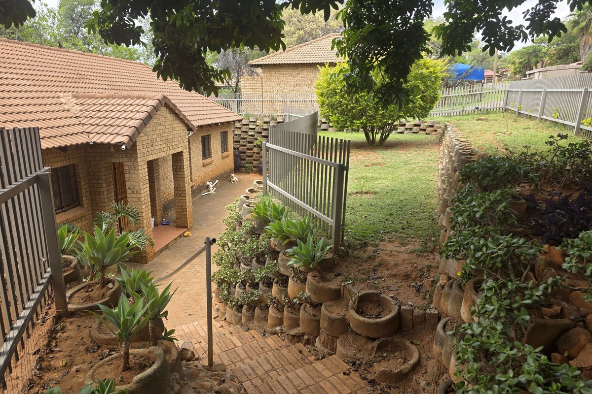 Rear exterior view featuring a brick house with a tiled roof, terraced garden with retaining walls, and a paved pathway leading to the entrance.