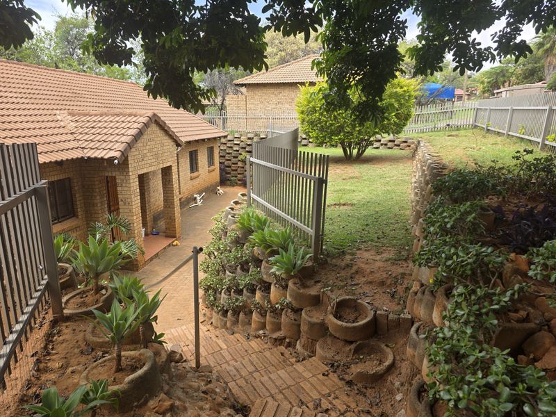 Rear exterior view featuring a brick house with a tiled roof, terraced garden with retaining walls, and a paved pathway leading to the entrance.
