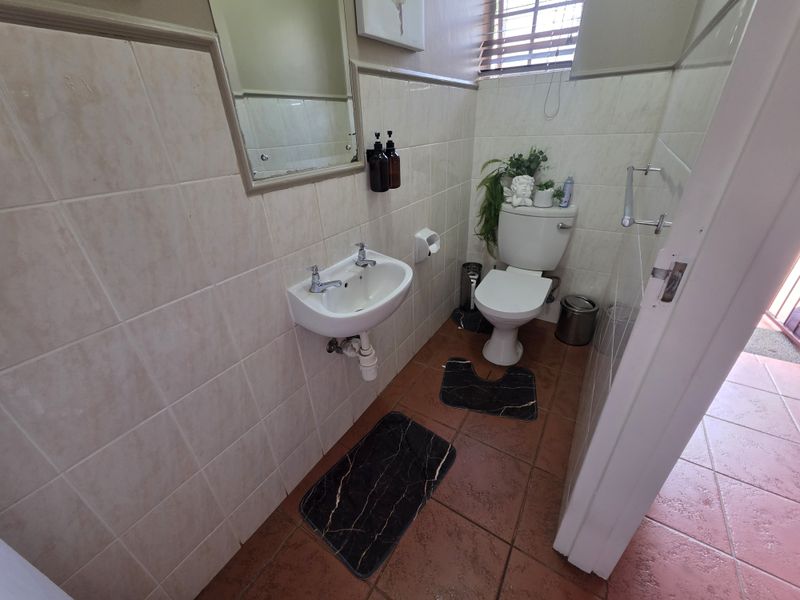 A compact guest bathroom featuring tiled walls and flooring, a wall-mounted basin, and a standard toilet.