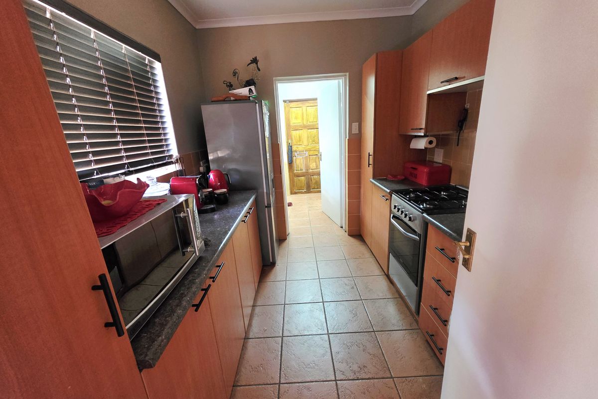 A functional galley-style kitchen featuring laminate cabinetry, stone-look countertops, a built-in oven with gas hob, and ceramic floor tiles.