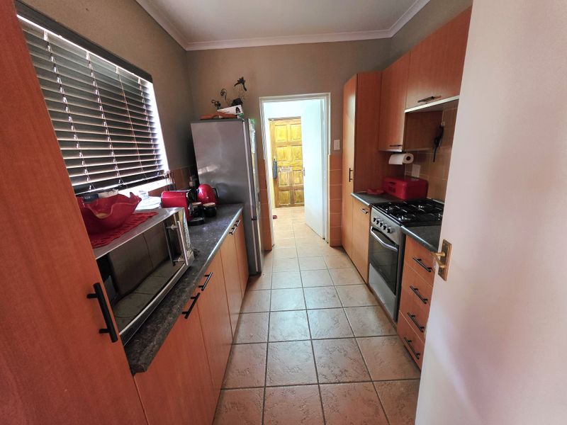 A functional galley-style kitchen featuring laminate cabinetry, stone-look countertops, a built-in oven with gas hob, and ceramic floor tiles.