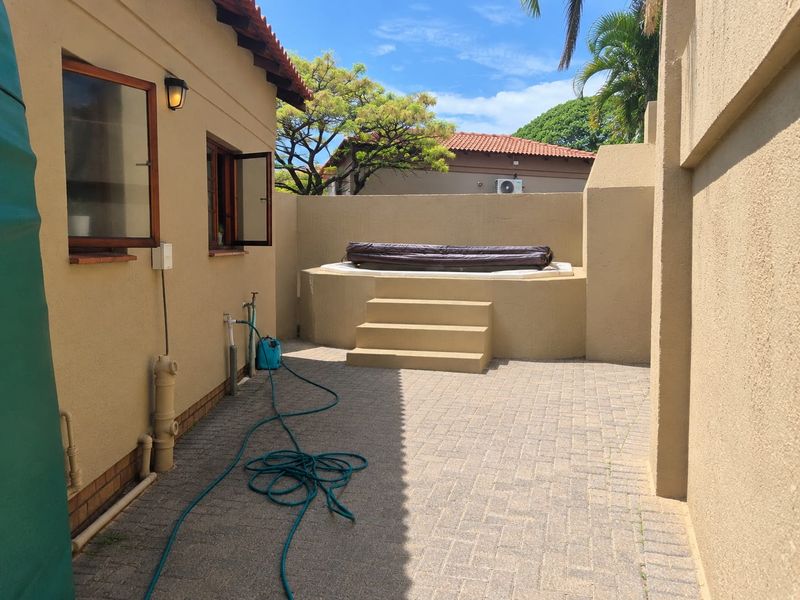 A private outdoor courtyard featuring a built-in spa with steps, paved flooring, and exterior wall lighting, providing a secluded relaxation space.