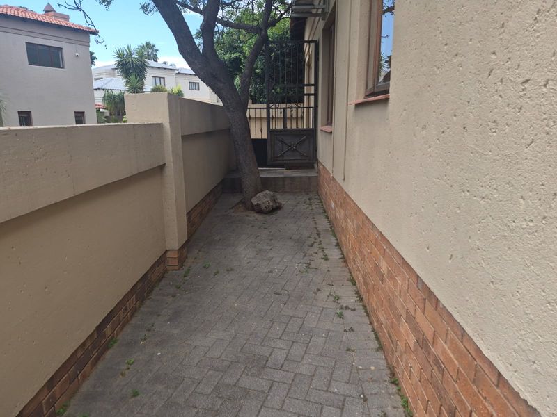 A narrow paved side passage featuring a boundary wall, brick exterior finish, and a secure metal gate.
