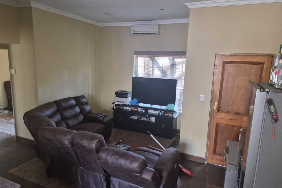 A living room featuring tiled flooring, air conditioning, and a wooden door, providing a functional space with neutral wall tones.