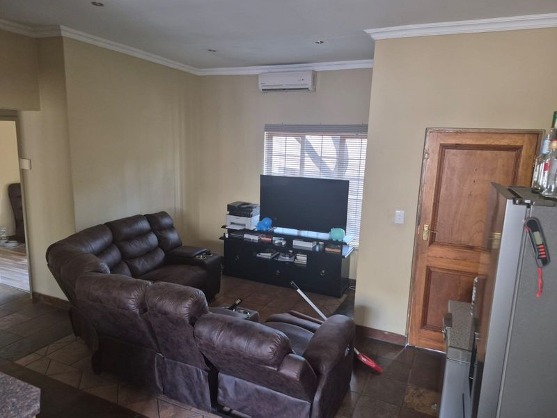 A living room featuring tiled flooring, air conditioning, and a wooden door, providing a functional space with neutral wall tones.
